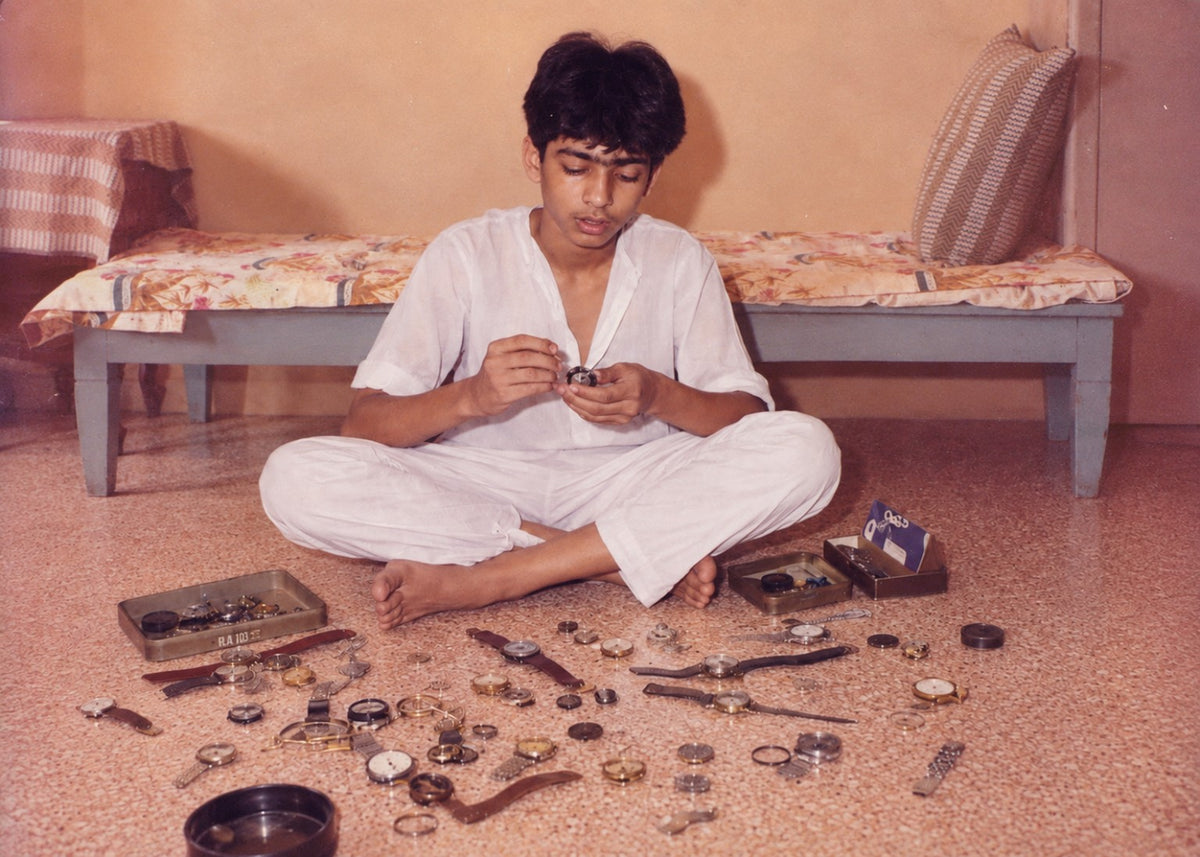 A young Siddhartha seated on the floor, surrounded by opened watches and watch parts